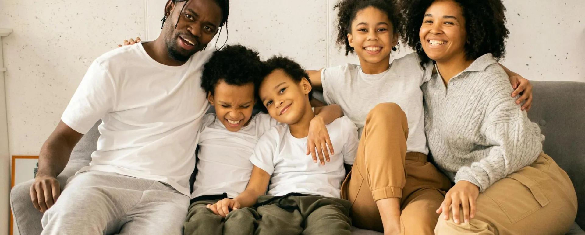 Full body of cheerful African American parents with children looking at camera while sitting on sofa in room with fireplace