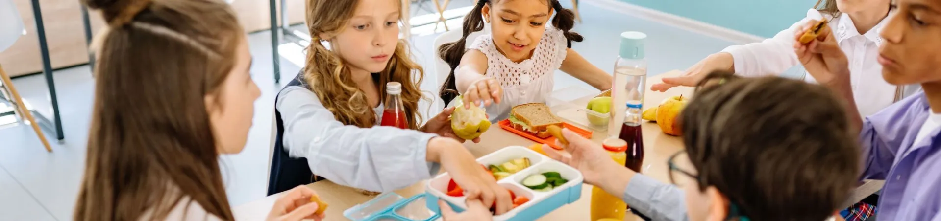 Group of diverse children having lunch in a school canteen, sharing and enjoying healthy snacks.