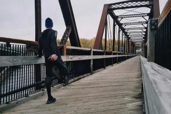 Man stretching on a wooden footbridge during a daytime run on an iron bridge, emphasizing fitness and recreation.