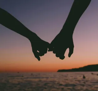 Silhouetted hands holding at sunset over a calm ocean. Romantic and peaceful seascape.
