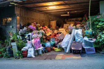 A garage filled with various household items, plants, and clutter overflowing onto the street.
