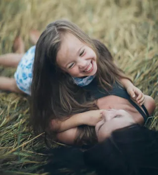 A joyful mother and daughter sharing a playful moment in a sunlit summer field.