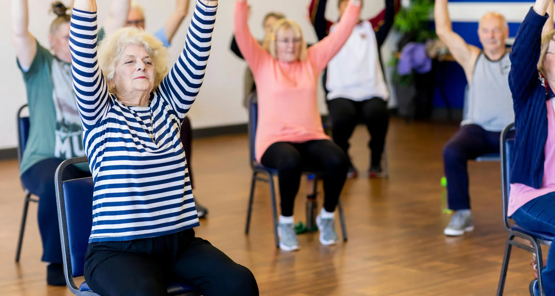 Group of senior adults participating in a chair exercise class, promoting fitness and healthy lifestyle.