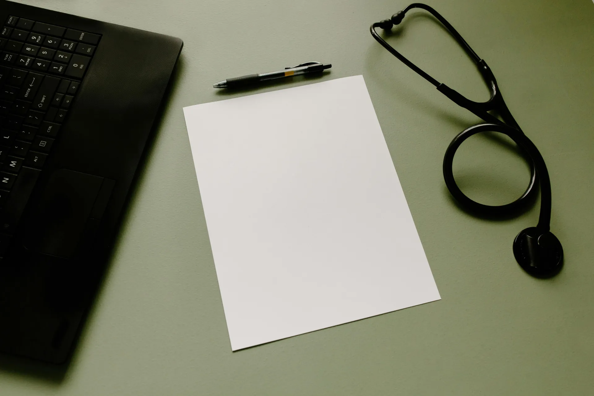Professional workspace featuring a laptop, stethoscope, pen, and paper sheet for healthcare tasks.