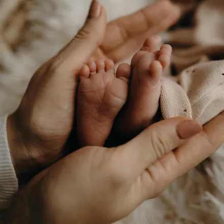 A close-up of a newborn's feet gently held by an adult's hands, symbolizing care and love.