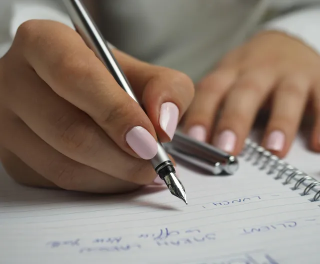 A detailed image of handwriting in a notebook with a fountain pen and glasses, ideal for office themes.