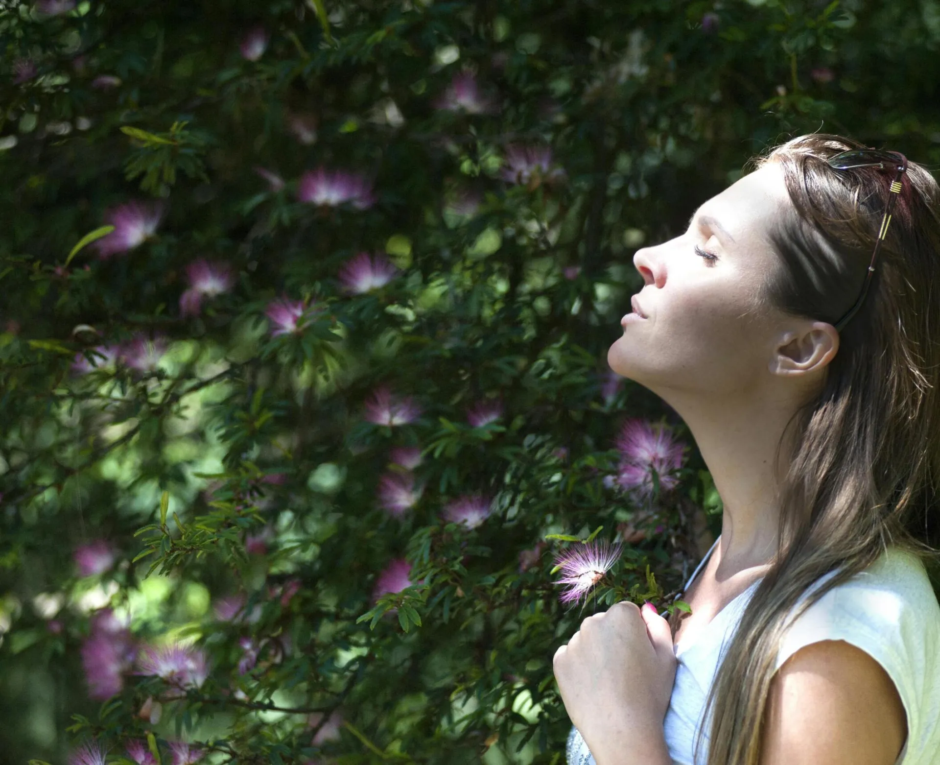 A woman enjoying a serene moment in a sunlit garden, surrounded by vibrant flowers.