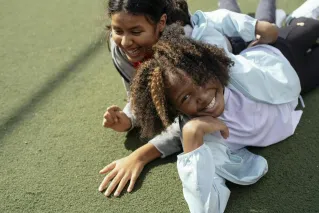 Cheerful multiracial girls lying on sports ground and smiling while spending sunny day together