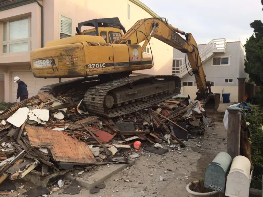 Large yellow bulldozer atop wreckage of a demolished beach shack