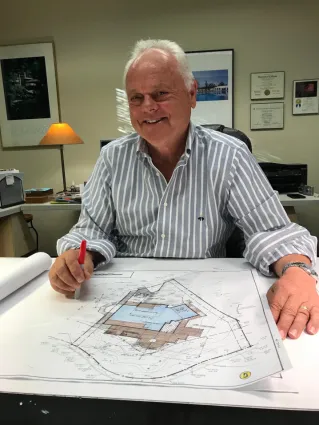 Smiling man seated at a desk with color blueprints in front of him