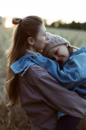 A heartwarming outdoor portrait of a mother lovingly holding her daughter during a peaceful day.