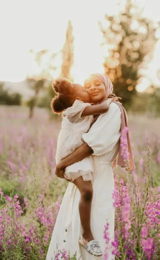 Mother and child in a loving embrace surrounded by blooming flowers in a summer meadow.