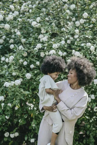 A mother and daughter share a joyful moment surrounded by lush white flowers in a sunny garden.