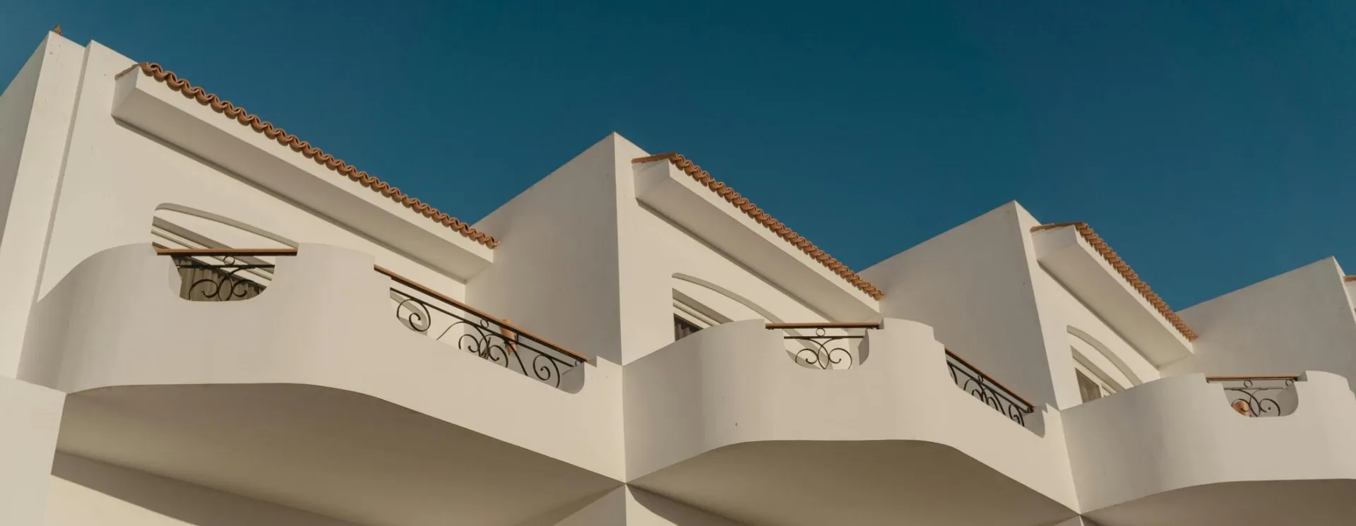 Elegant white Mediterranean building with ornate balconies under a clear blue sky.