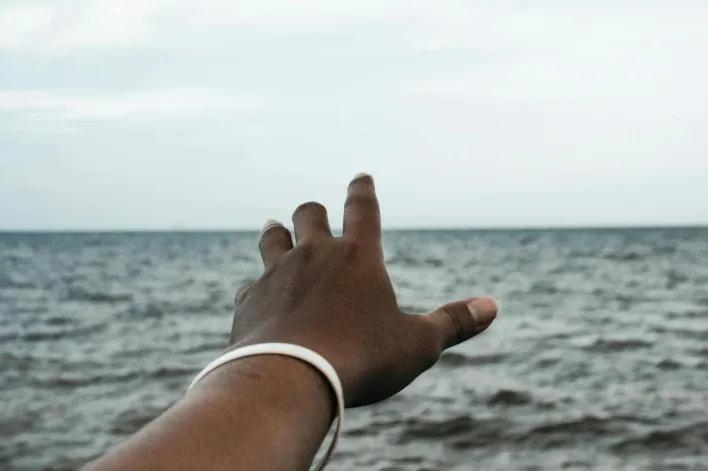 A hand reaching towards the horizon over the sea, signifying aspiration.