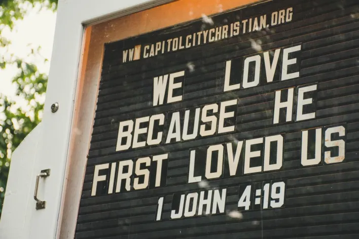 Church sign displaying biblical verse about love from 1 John 4:19 in outdoor setting.