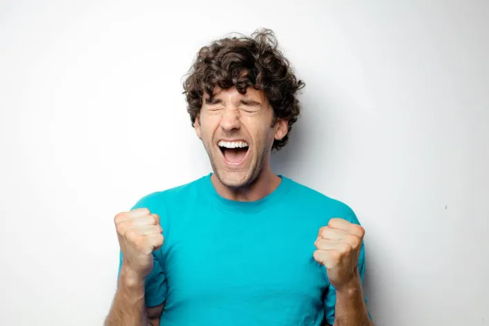 Portrait of a joyful man in a blue shirt celebrating with excitement and closed eyes.