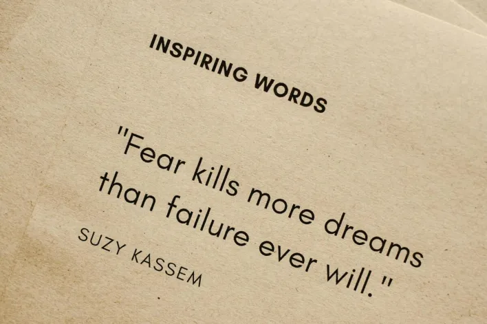 Motivational quote 'Fear kills more dreams than failure ever will.' by Suzy Kassem on paper texture.