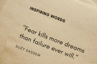 Motivational quote 'Fear kills more dreams than failure ever will.' by Suzy Kassem on paper texture.