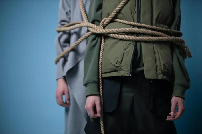 Two individuals tangled in rope symbolize unity or conflict against a blue backdrop.