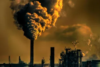 A factory emitting smoke clouds against a dark sunset sky, illustrating air pollution and industrial impact.