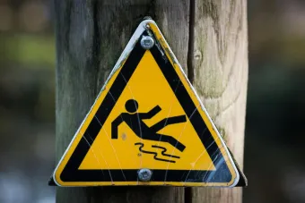 Close-up of a triangular warning sign indicating a slippery surface, fixed to a wooden post.