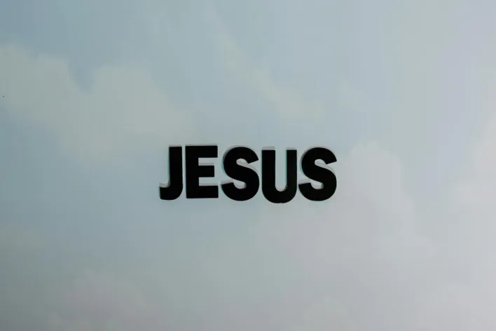 Minimalist image with bold 'JESUS' text against a cloudy sky background.
