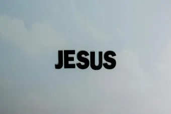 Minimalist image with bold 'JESUS' text against a cloudy sky background.