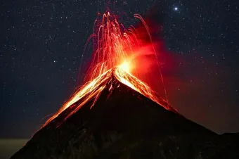 A breathtaking view of a volcano eruption with glowing lava against a starry night sky.