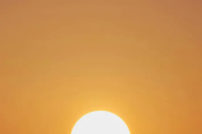 A vibrant sunset with a vivid orange sky and a prominently setting sun.