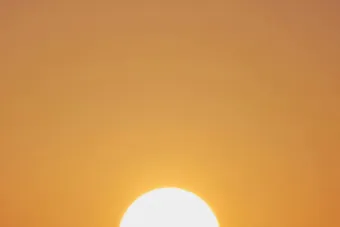 A vibrant sunset with a vivid orange sky and a prominently setting sun.