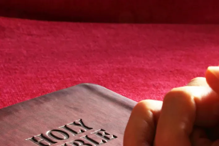 Close-up of hands praying on a Holy Bible, symbolizing faith and spirituality.