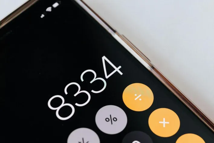 From above of modern cellphone in metal frame with open calculator application representing circles with numbers and symbols on black screen
