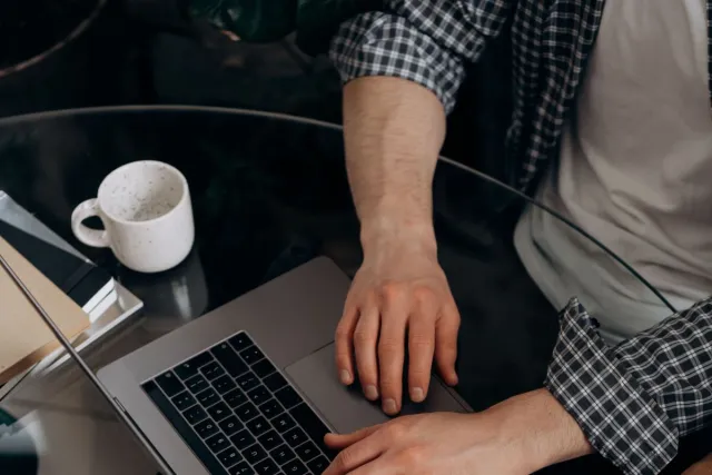 Two people using laptops at a glass table, top view, showcasing teamwork.