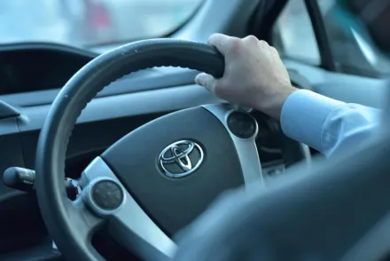 Close-up view of a hand gripping a Toyota steering wheel in a car interior, Faisalabad, Pakistan.