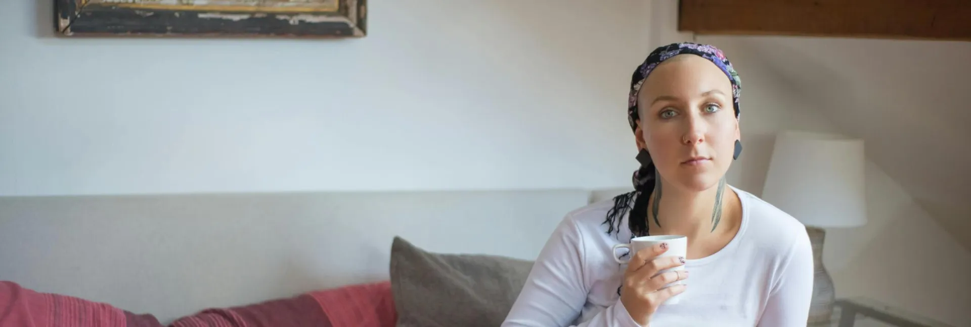 A woman in a headscarf sits on a sofa indoors enjoying a coffee.