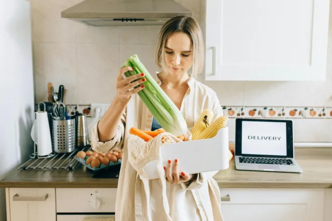 A Pop In Concierge unpacks fresh vegetables from delivery box in a modern kitchen setup