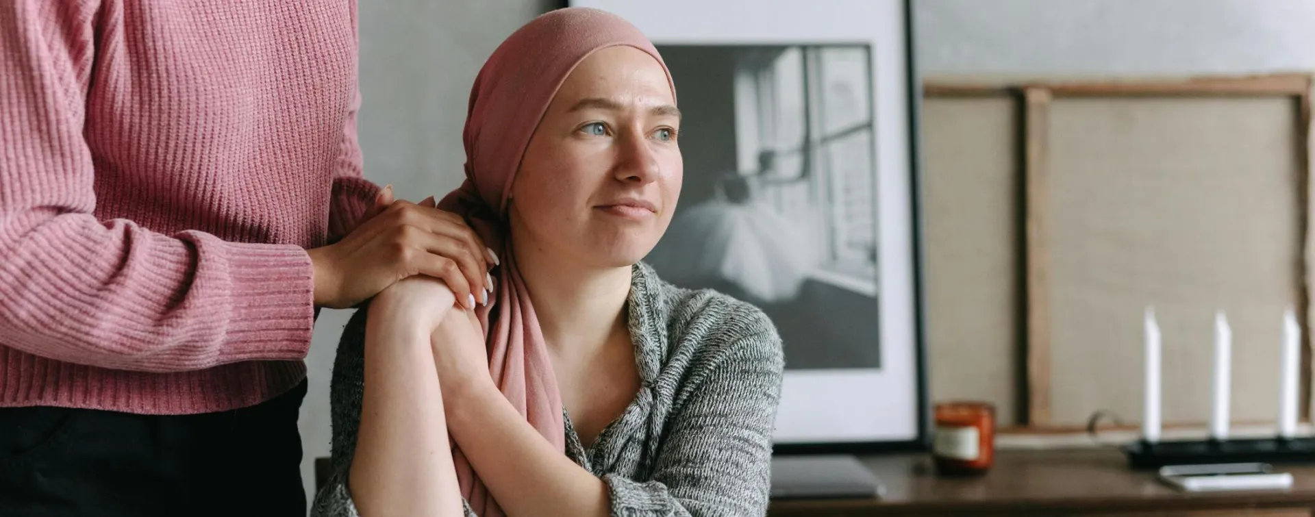 A supportive moment indoors featuring a cancer patient comforted by a friend, conveying emotion and care.