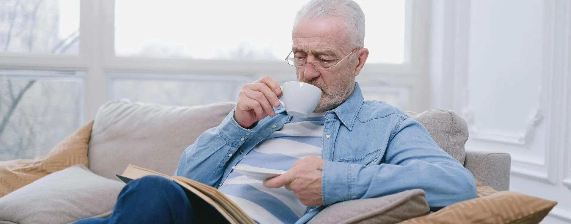 Elderly man enjoying a peaceful moment on sofa with a hot drink and book after hiring the Pop In Conierge Service