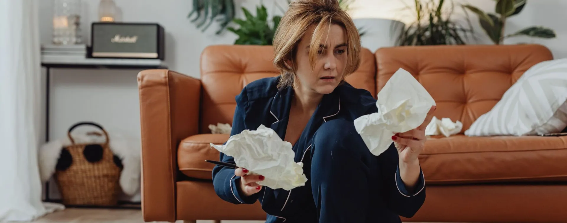 A woman in comfortable loungewear surrounded by crumpled papers, working remotely from home.