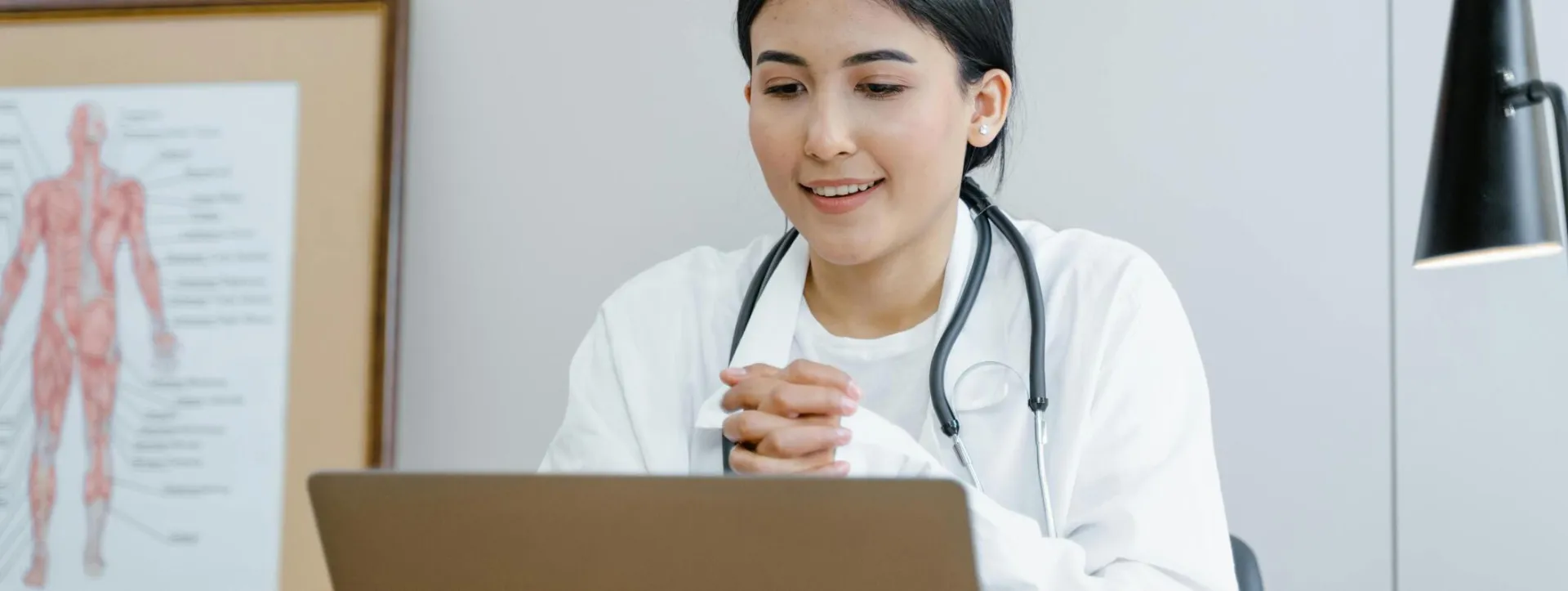 A young female doctor smiling while engaging in a telemedicine session on her laptop.
