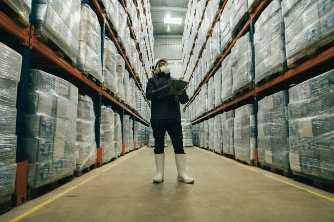 Man in beanie inspects warehouse drum, using a tablet for inventory.