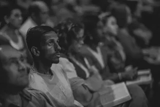 A monochrome photograph of a focused man in a diverse audience setting.