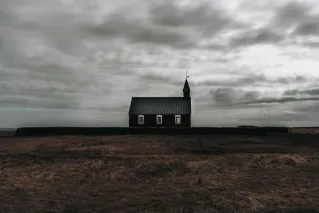 Minimalist view of a solitary church set against a moody sky, surrounded by rural fields.