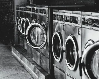 A row of industrial washing machines in an urban laundromat, showcasing steel finish.
