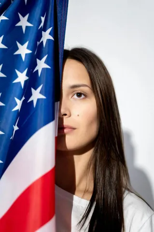 Elegant portrait of a woman partially hidden by an American flag, symbolizing patriotism.