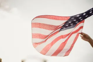 From below of crop anonymous patriot waving flag of United States of America against cloudy sky