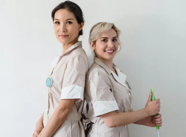 Two cleaning professionals standing back to back in uniform, ready for work.