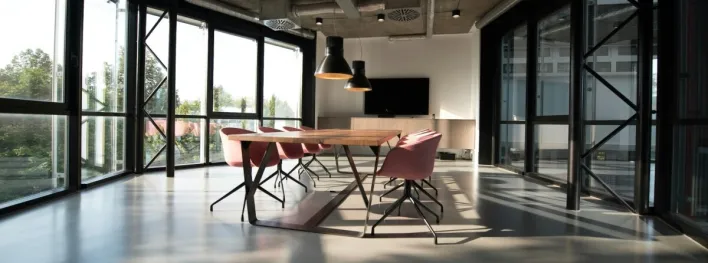 Spacious, sunlit office lounge featuring white tables and chairs with a modern aesthetic.
