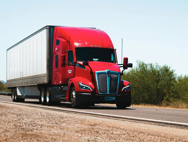 Vibrant red semi-trailer truck driving on an open highway under a clear blue sky.